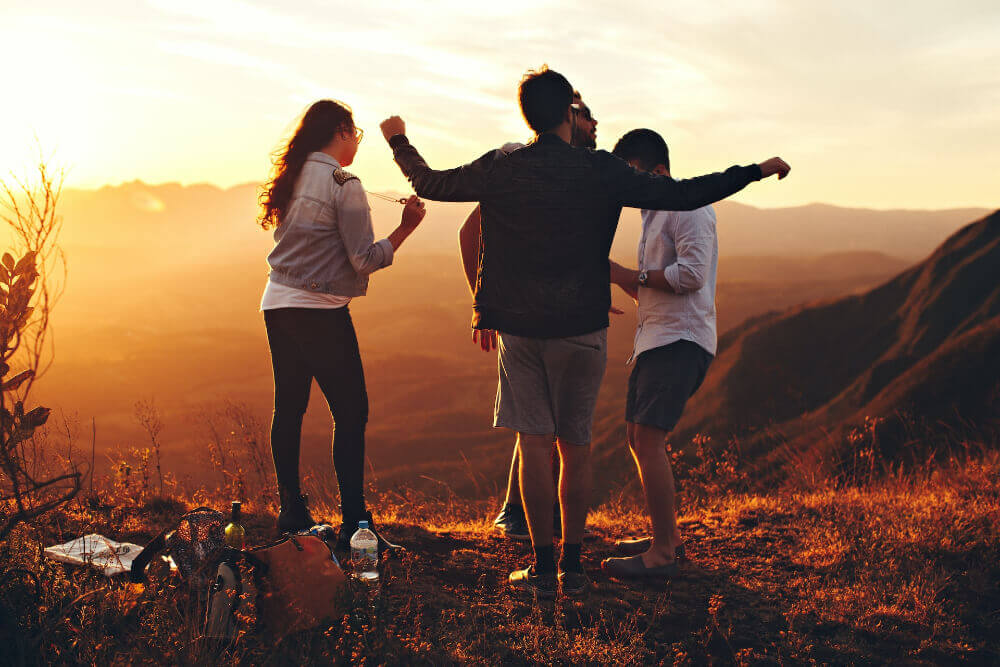 Four Person Standing at Top of Grassy Mountain Stock Photo