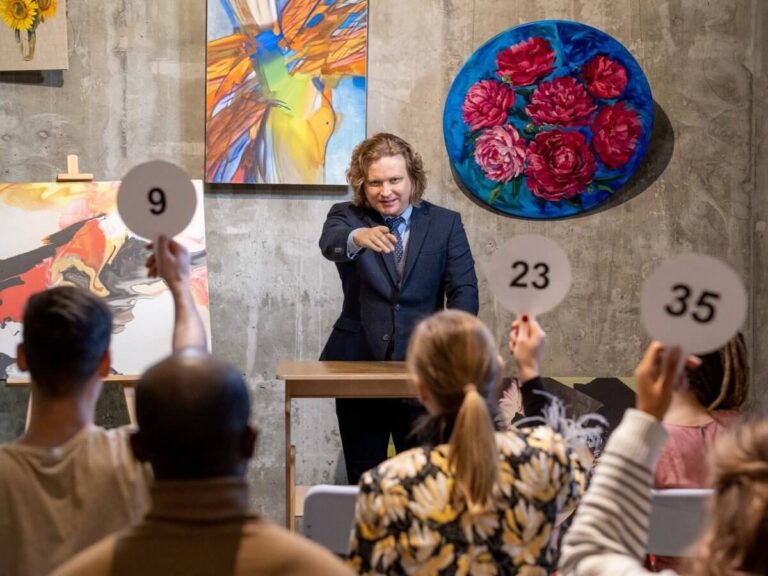 Auction company website design: auctioneer at the podium taking bids from an audience raising numbered paddles in a gallery