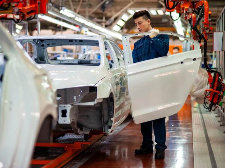 Auto manufacturer website design: automotive plant worker checking the door fit on a white car body moving down the assembly line
