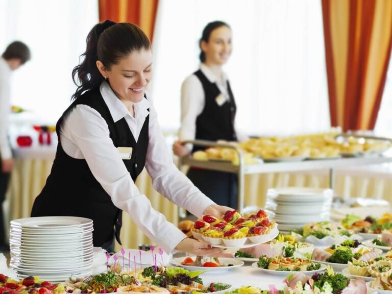 Catering company website design: smiling catering server placing a platter of fruit tarts on a buffet table at an event