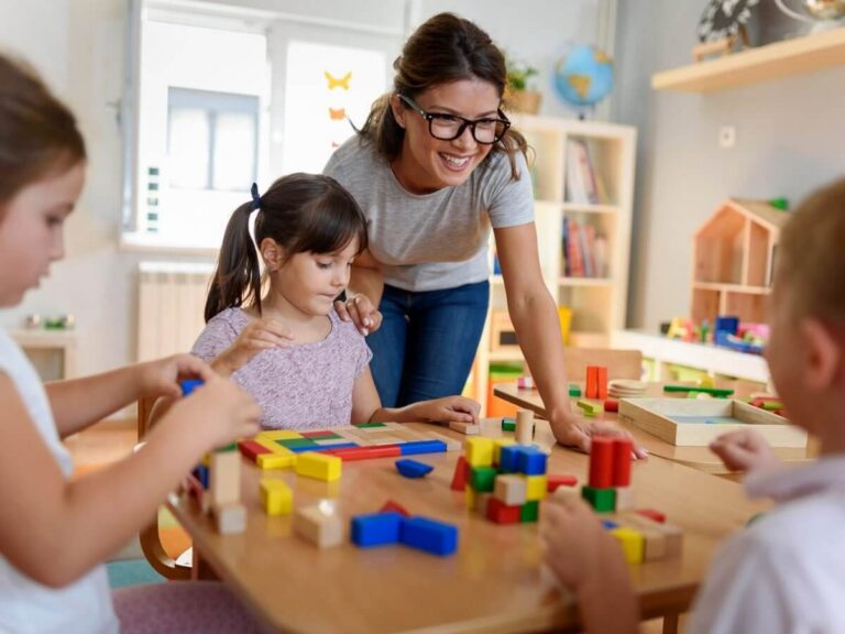 Child care center website design: smiling daycare teacher helping preschoolers build with colorful wooden blocks at a classroom table