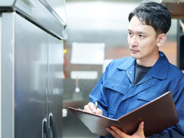 Commercial refrigeration website design: refrigeration technician checking a stainless steel reach-in cooler in a commercial kitchen and taking notes