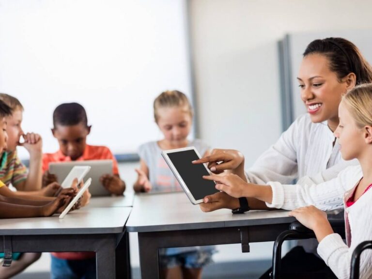 Edtech website design: teacher guiding a student on a tablet while classmates use tablets for a lesson in class