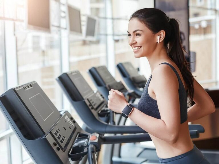 Fitness equipment brand website design: smiling woman running on a treadmill in a row of cardio machines at a bright gym