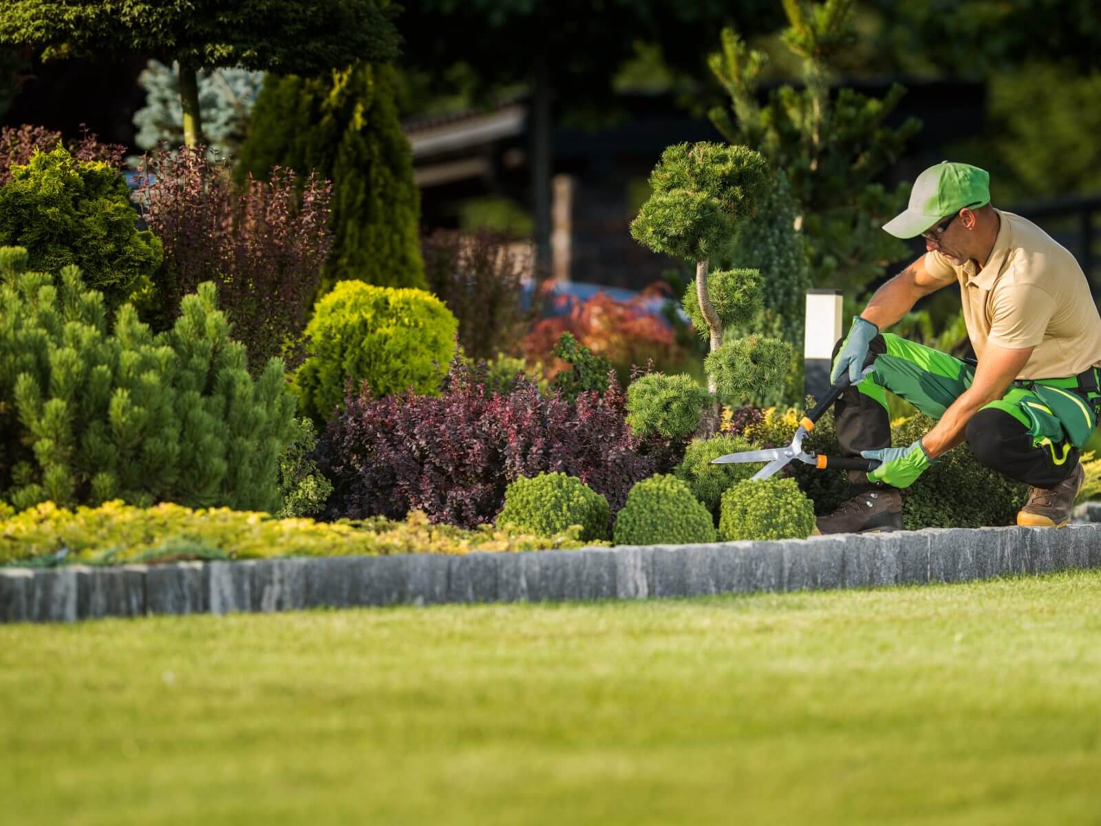 Landscaping company website design: landscaper trimming shrubs in a manicured front garden