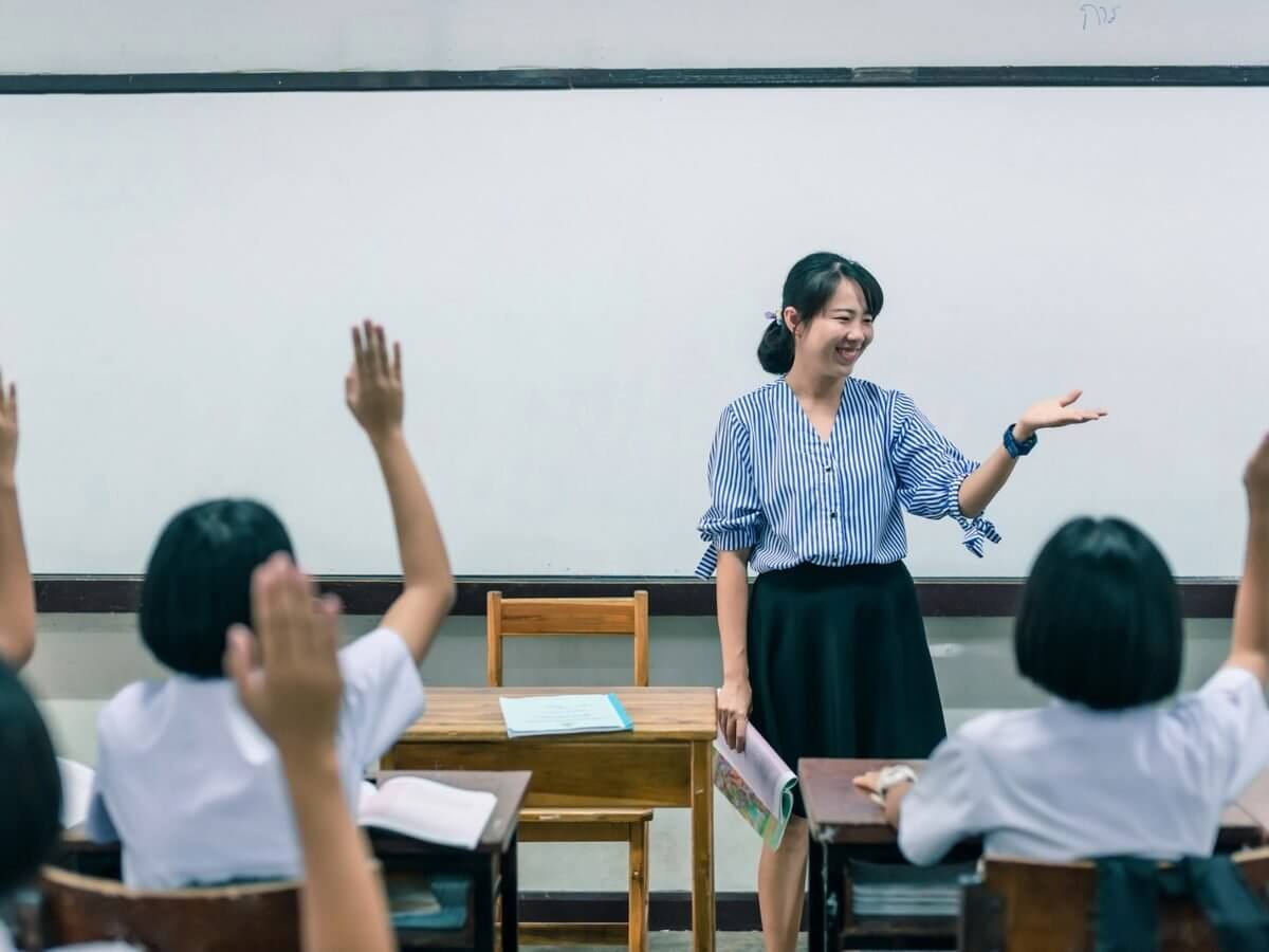 Private school website design: smiling teacher calling on uniformed students raising their hands in a private school classroom