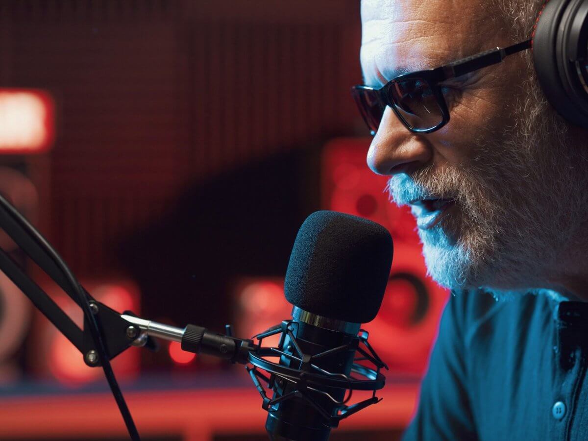 Radio station website design: radio host in headphones and glasses speaking into a studio microphone during a live broadcast