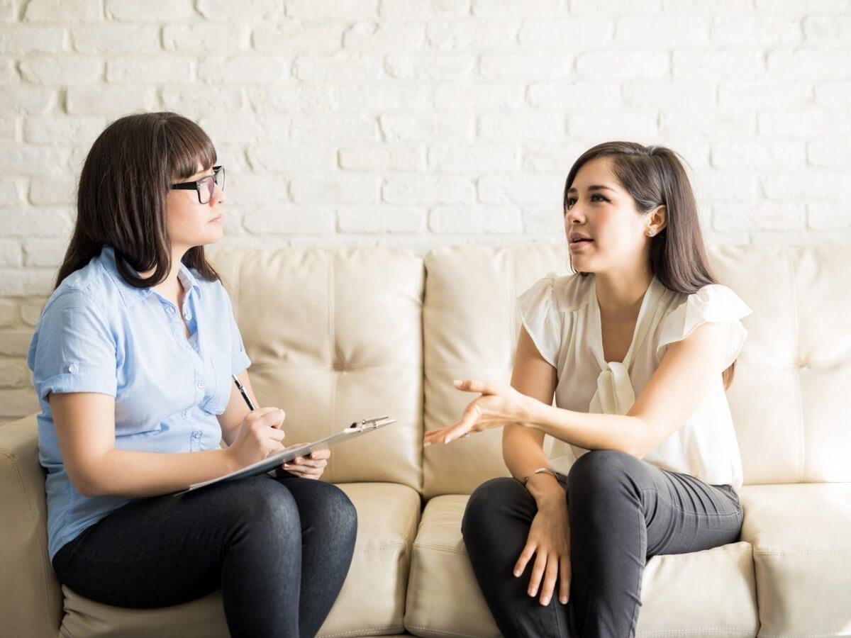 Therapist website design: therapist with a clipboard listening closely to a client during a counseling session on a cream sofa