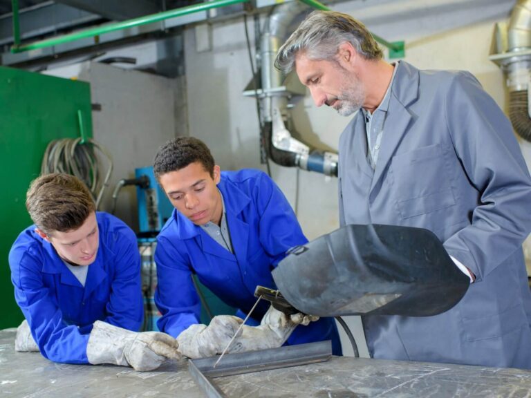 Trade school website design: instructor teaching two students metalwork in a training workshop