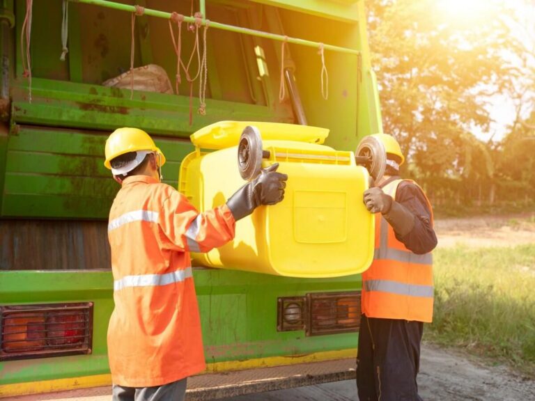 Waste management website design: sanitation crew in hard hats and high visibility gear lifting a yellow bin into a garbage truck